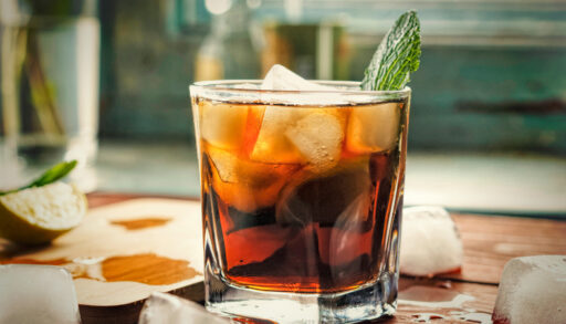 Glass of rum with a mint leaf in it on a wooden table.