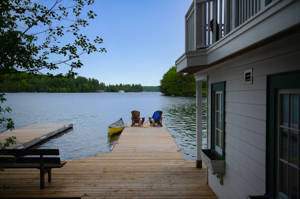 Two Adirondack chairs on a dock connected to a cabin both overlooking a lake.