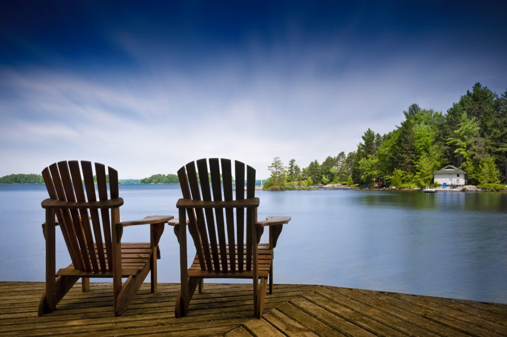 Muskoka chairs on a dock overlooking a lake.