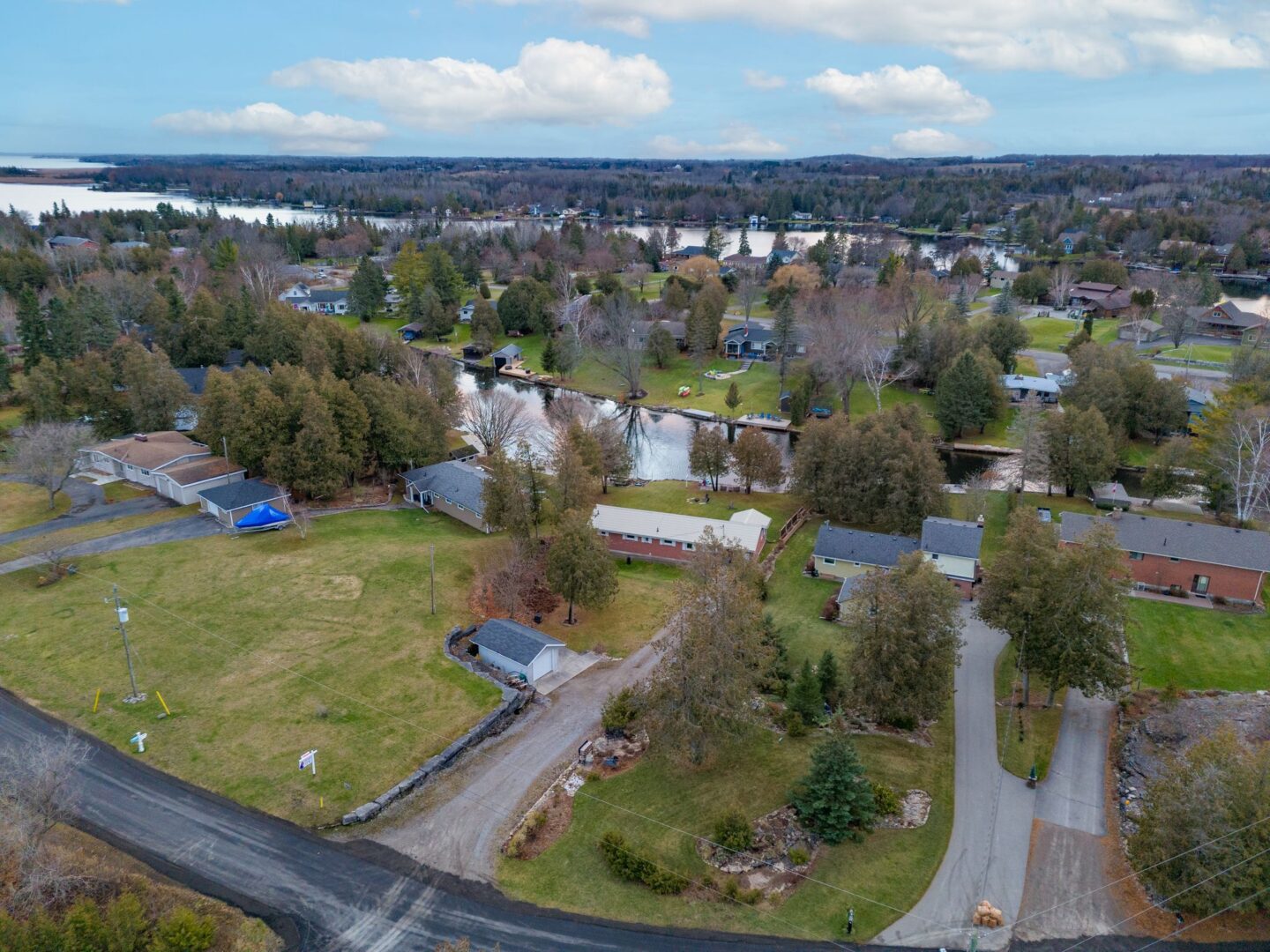 Overhead view of a residential street on a river. A bungalow with a long driveway sits in the middle of the street.