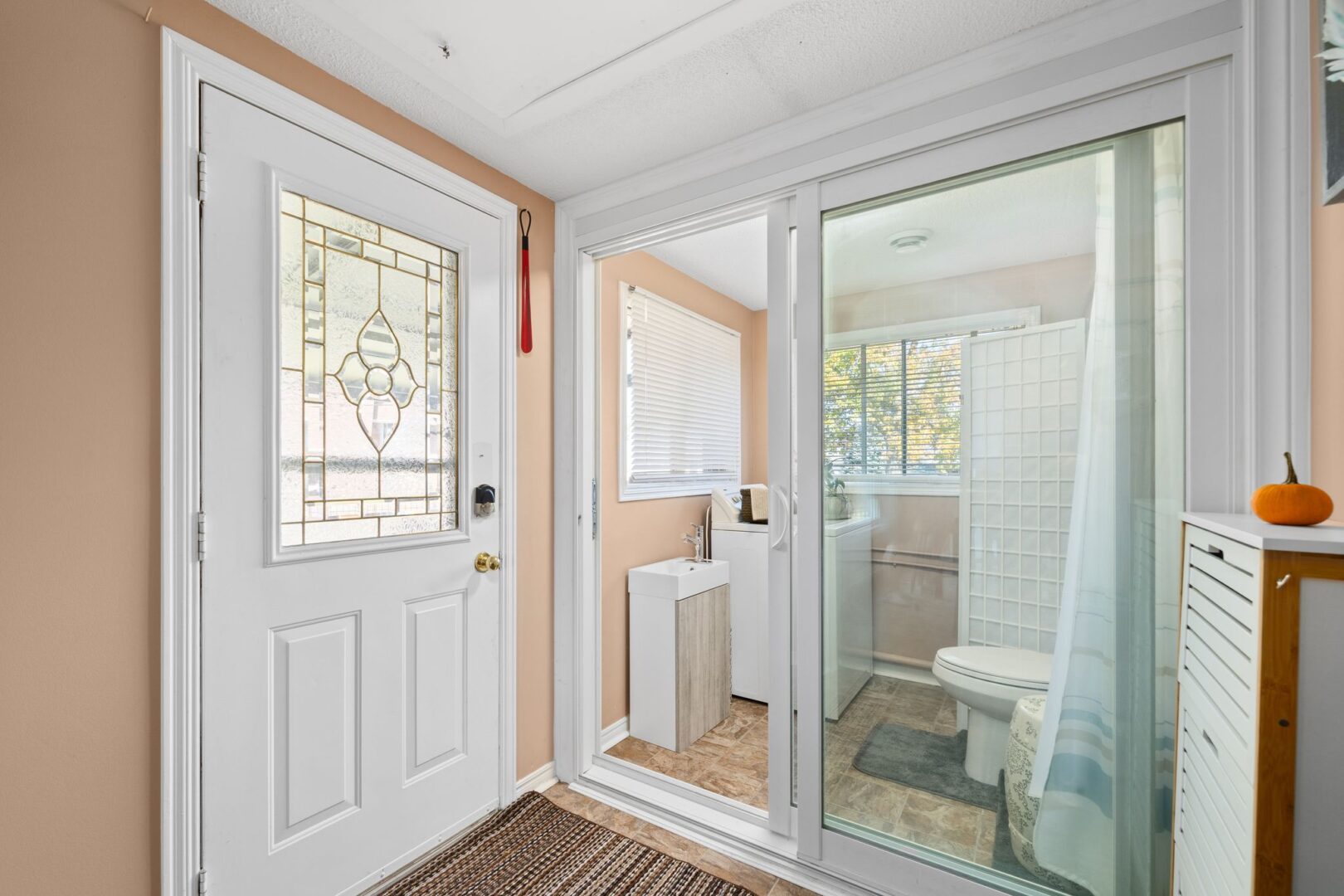 Inside the bright front entrance of a bungalow. Just beside the front door are two glass doors leading to a joint bathroom and laundry area, with a curtain that can pull across the doors from the inside.