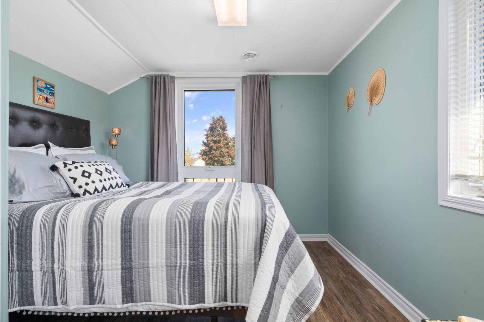 A bedroom with dark wood floors, light blue walls, and a big bed.