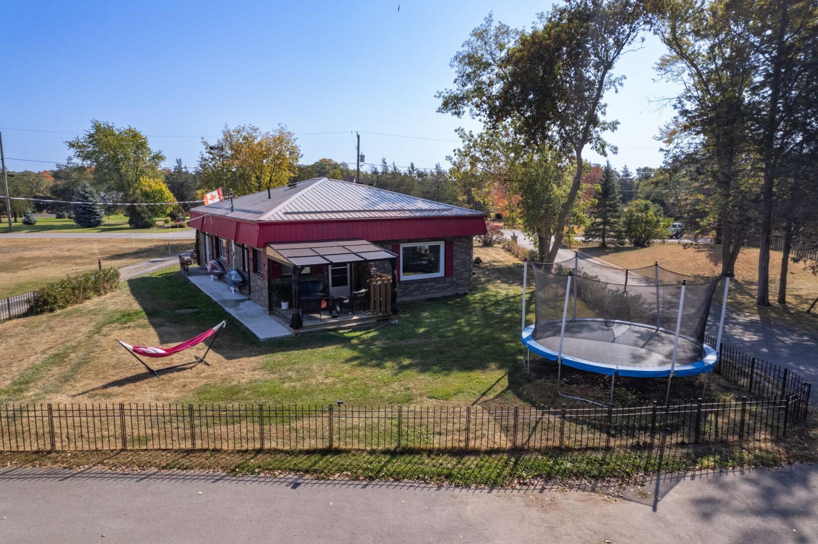 A small bungalow with a red roof, red window trim, and a grassy yard. A round trampoline sits in a corner of the yard.