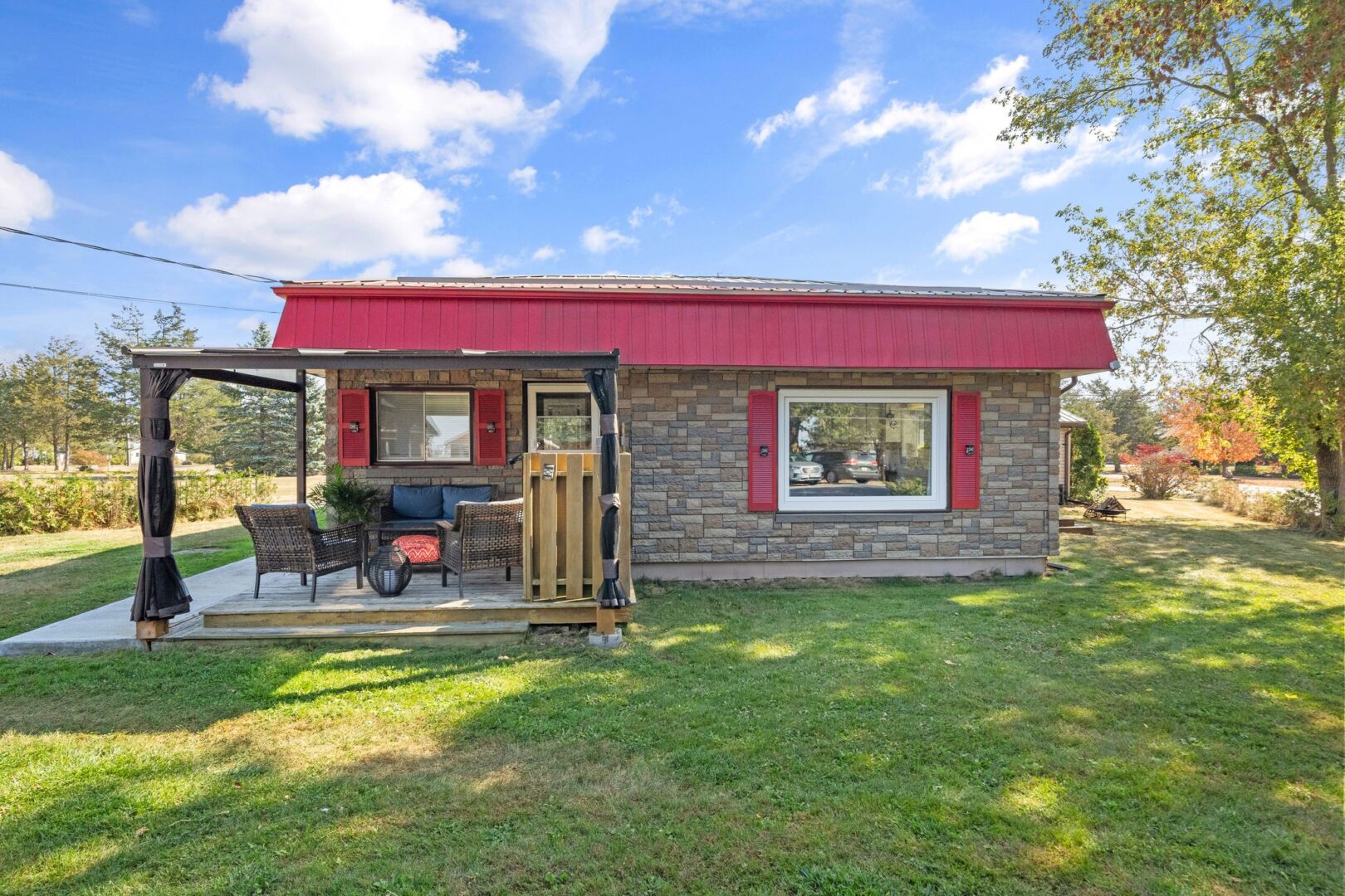 The back of a small bungalow with red roof and window trim. A covered deck with outdoor seating extends off the back of the home.