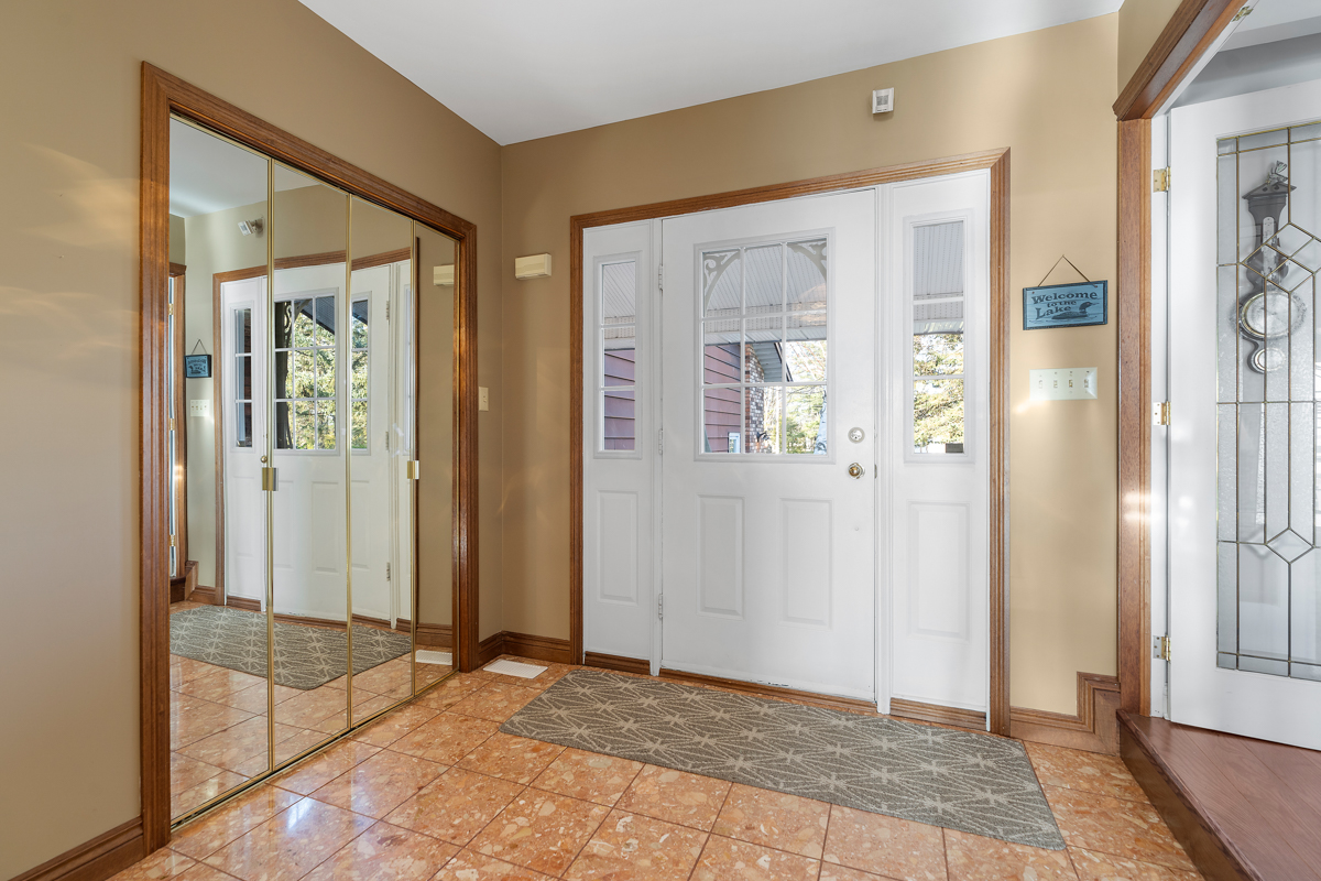Inside the front door of a home. A double-door closet with mirrors reflects the white front door. The floors are shiny, terracotta-coloured tile.