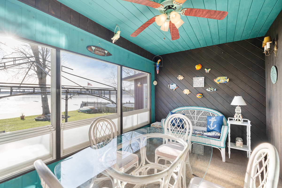 A sunroom with bright turqoise walls, large windows, a ceiling fan, and a clear glass table surrounded by white wicker chairs. One accent wall is painted black and decorated with colourful fish.