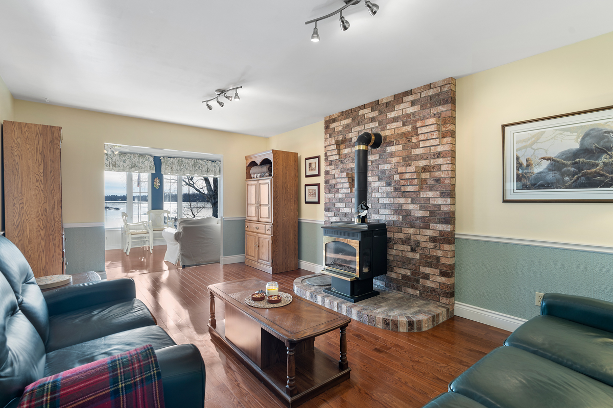 A cozy living area with cushy, dark green couches and hardwood floors. A wood stove sits on one side of the room, on floor-to-ceiling stone.