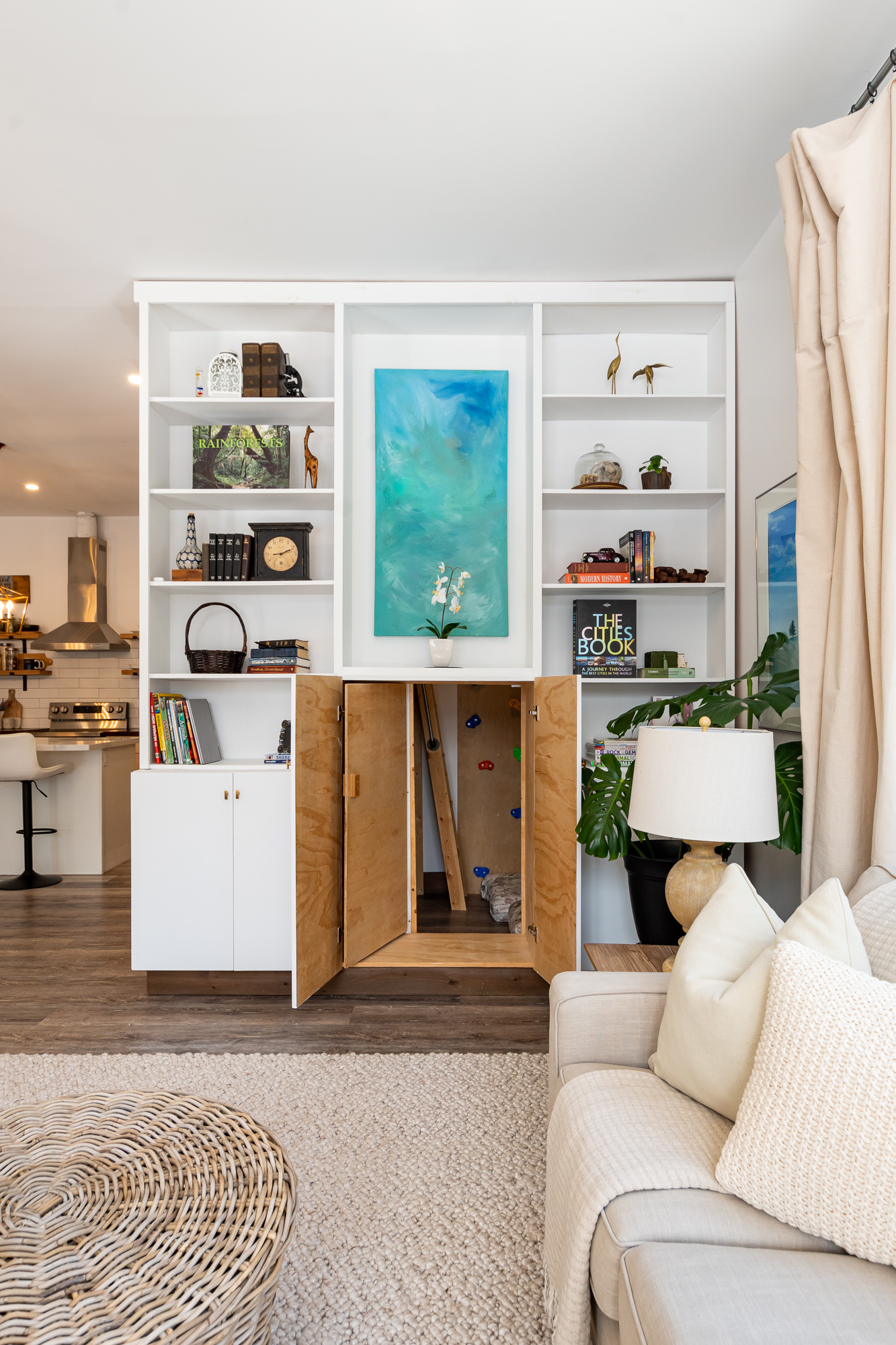 A white bookshelf with books and decor on it. In the middle, a cabinet opens to reveal a wood-panelled room inside