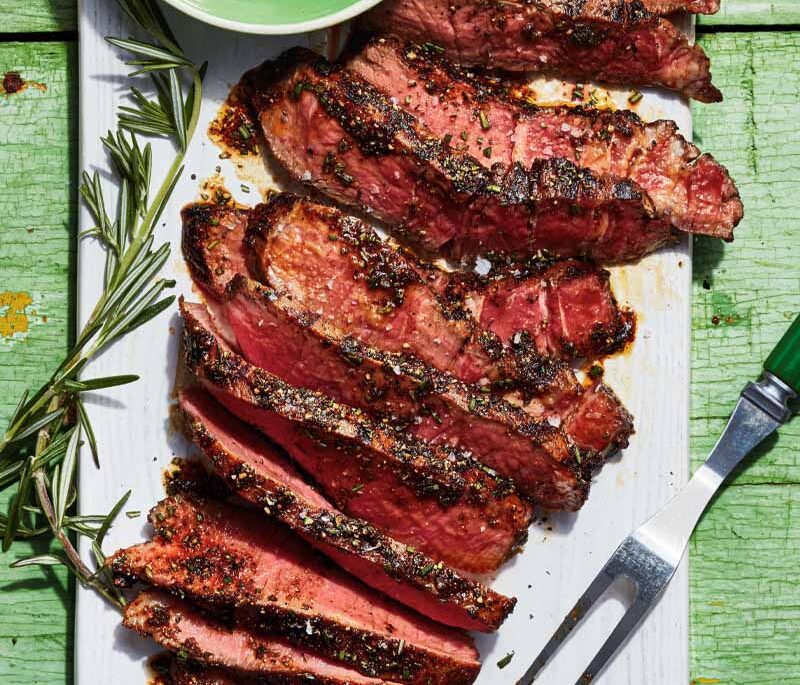 Sliced steak on a white plate with a small green bowl of spice