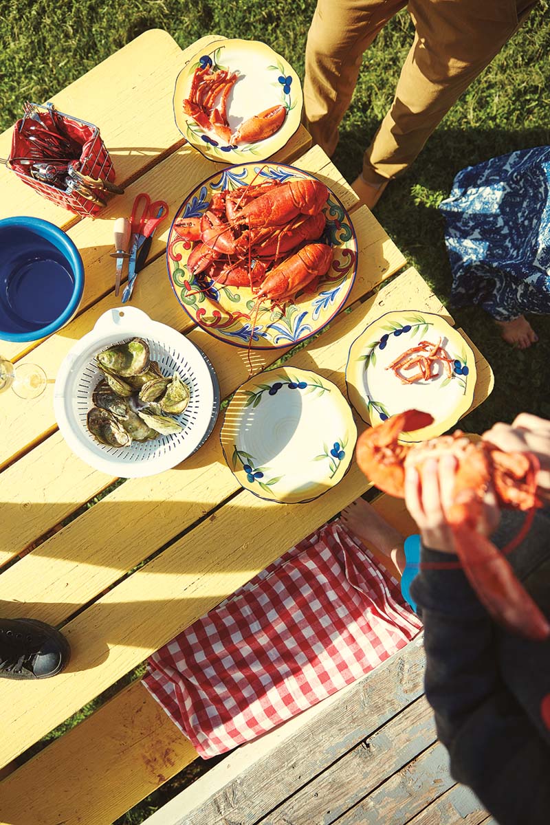 A yellow picnic table with plates of bright red lobster and seafood
