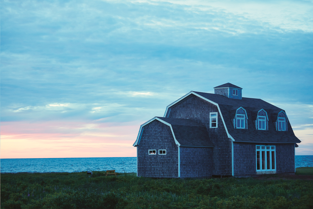 A barn-style cottage sits on the edge of a cliff in front of a sunset