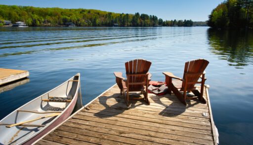 A shot of a dock with two Muskoka chairs and a canoe