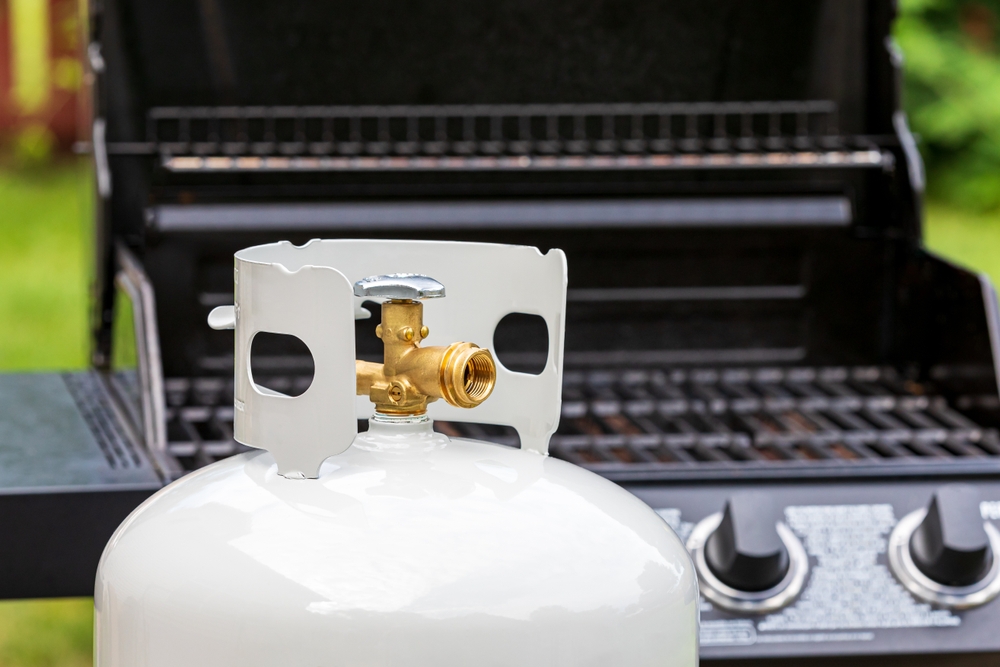 A propane tank with a barbecue in the background