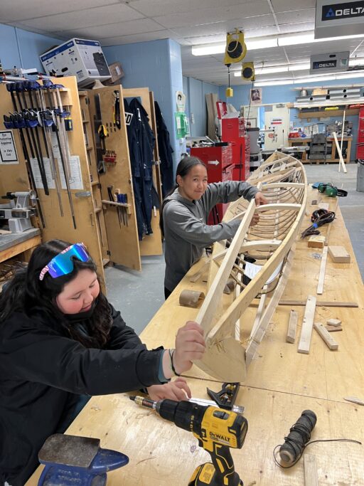 Two people building the wood frame of a kayak