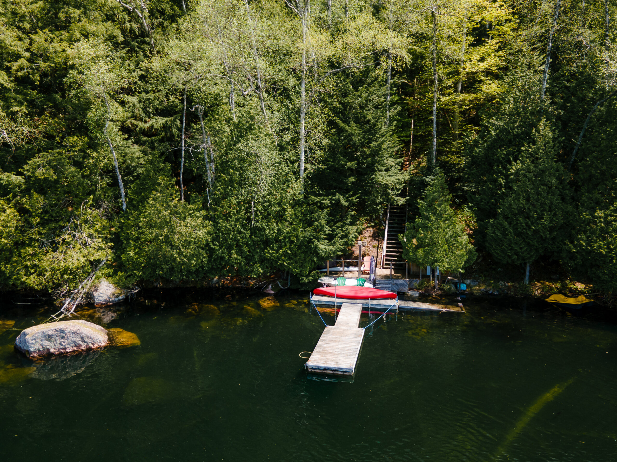 Aerial view of a dock in blue water. The dock leads up into the forest behind