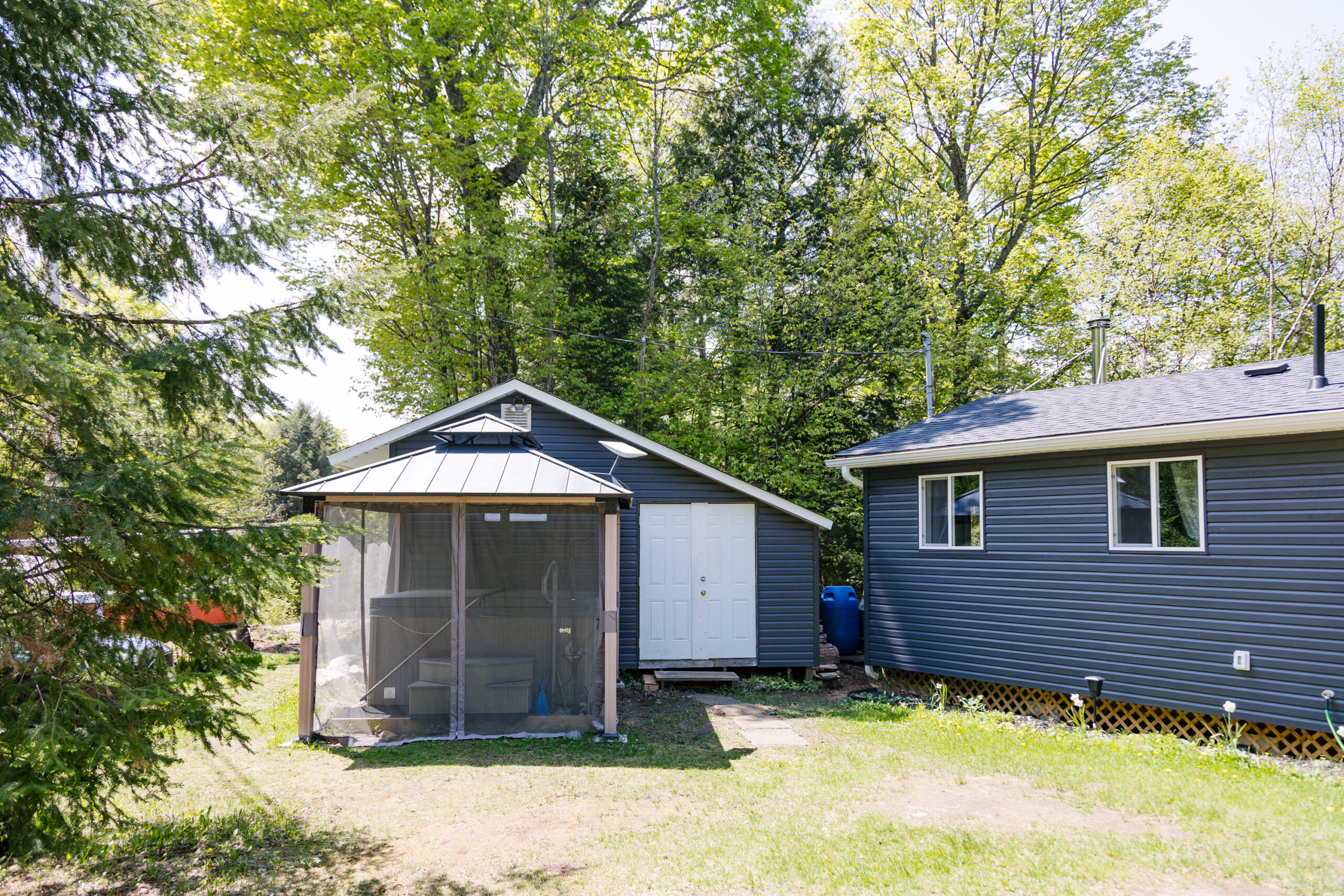 A blue-grey panelled shed with a white door. A hot tub is covered by a mesh covered gazebo