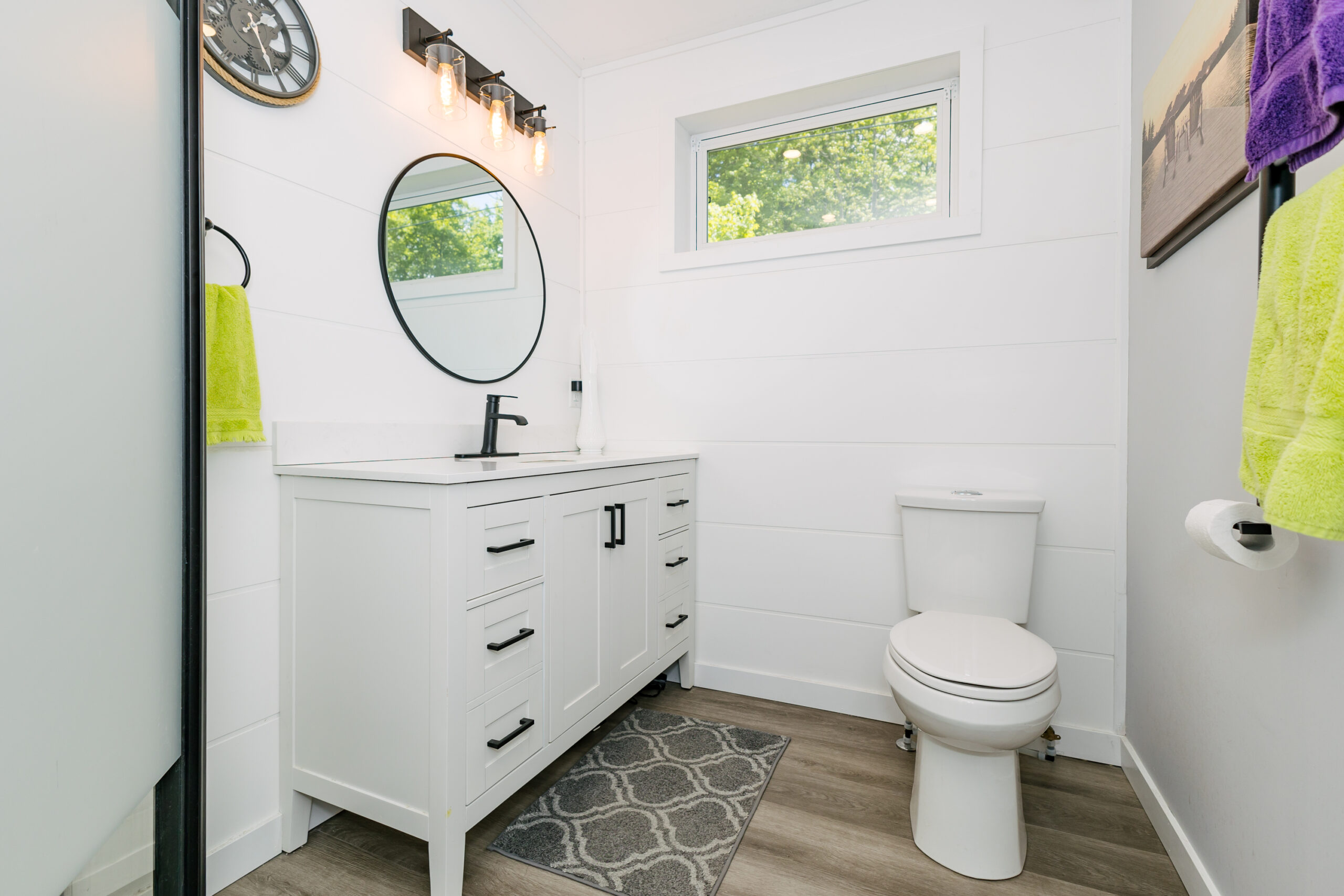 A white bathroom cabinet with a round mirror above, next to a white toilet