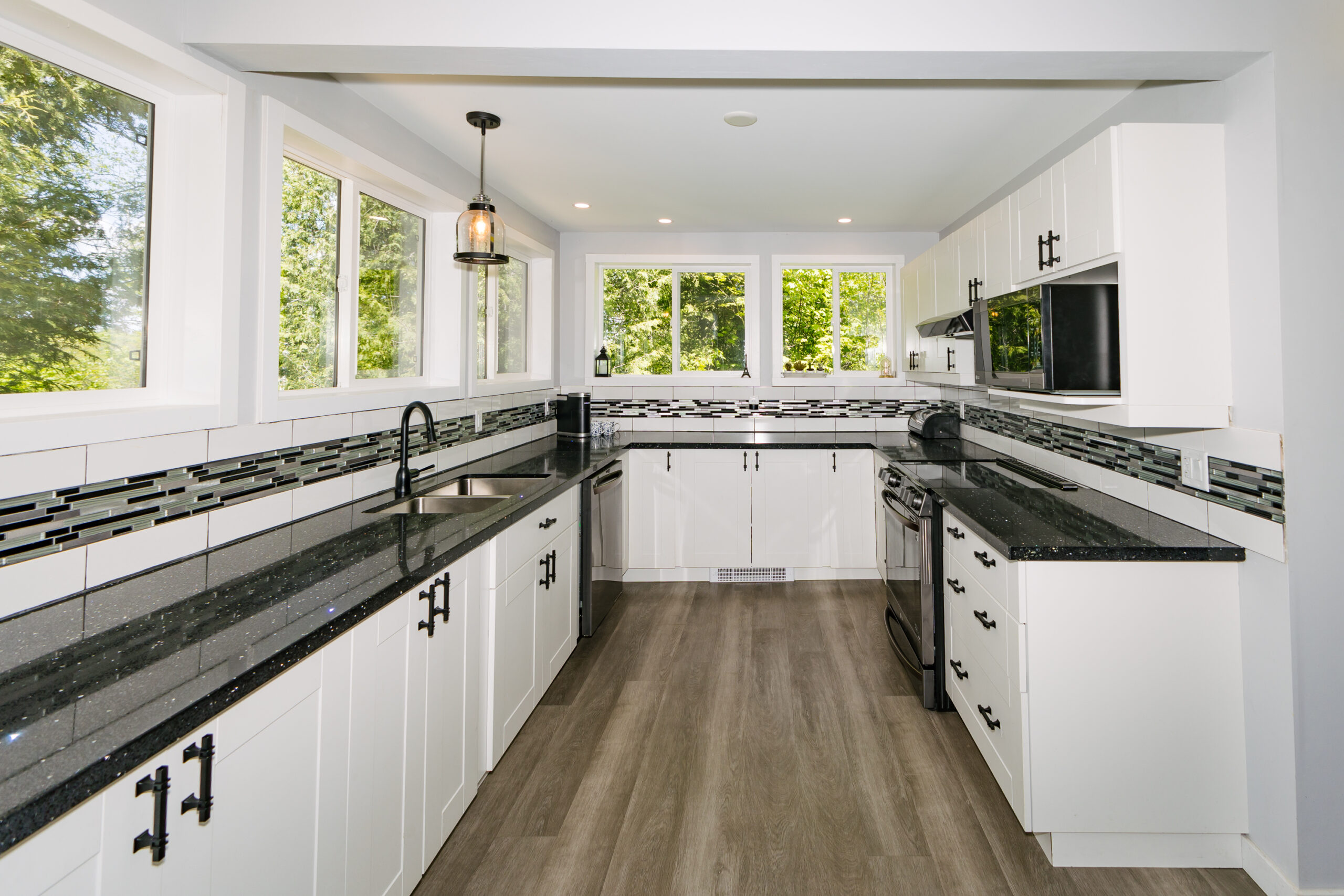 Wraparound white lower kitchen cabinets with black countertops. Windows above the counters