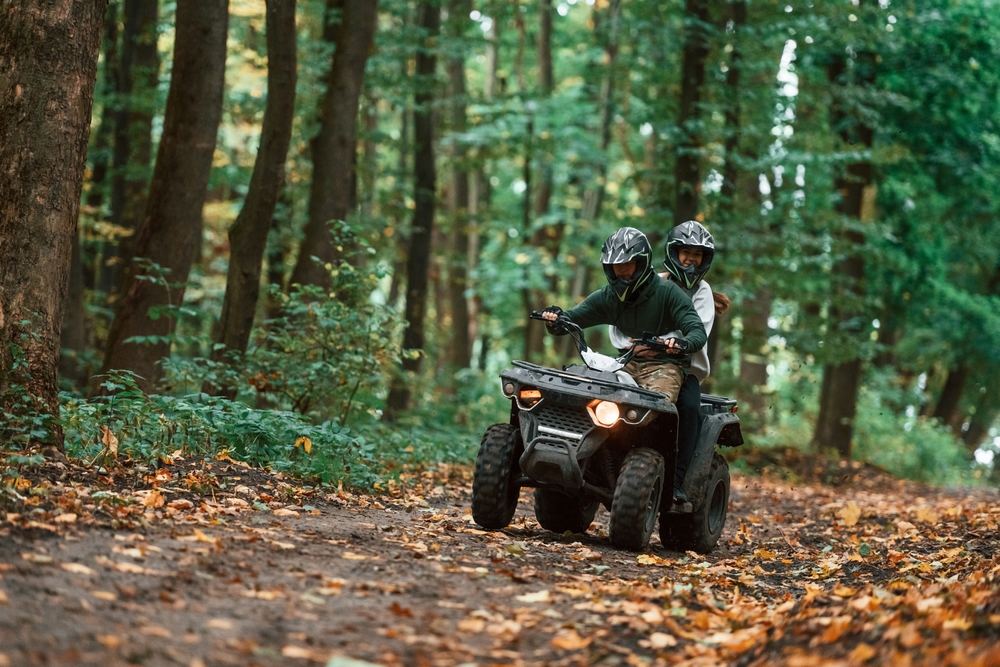 Two passengers riding an ATV on a trail in the woods