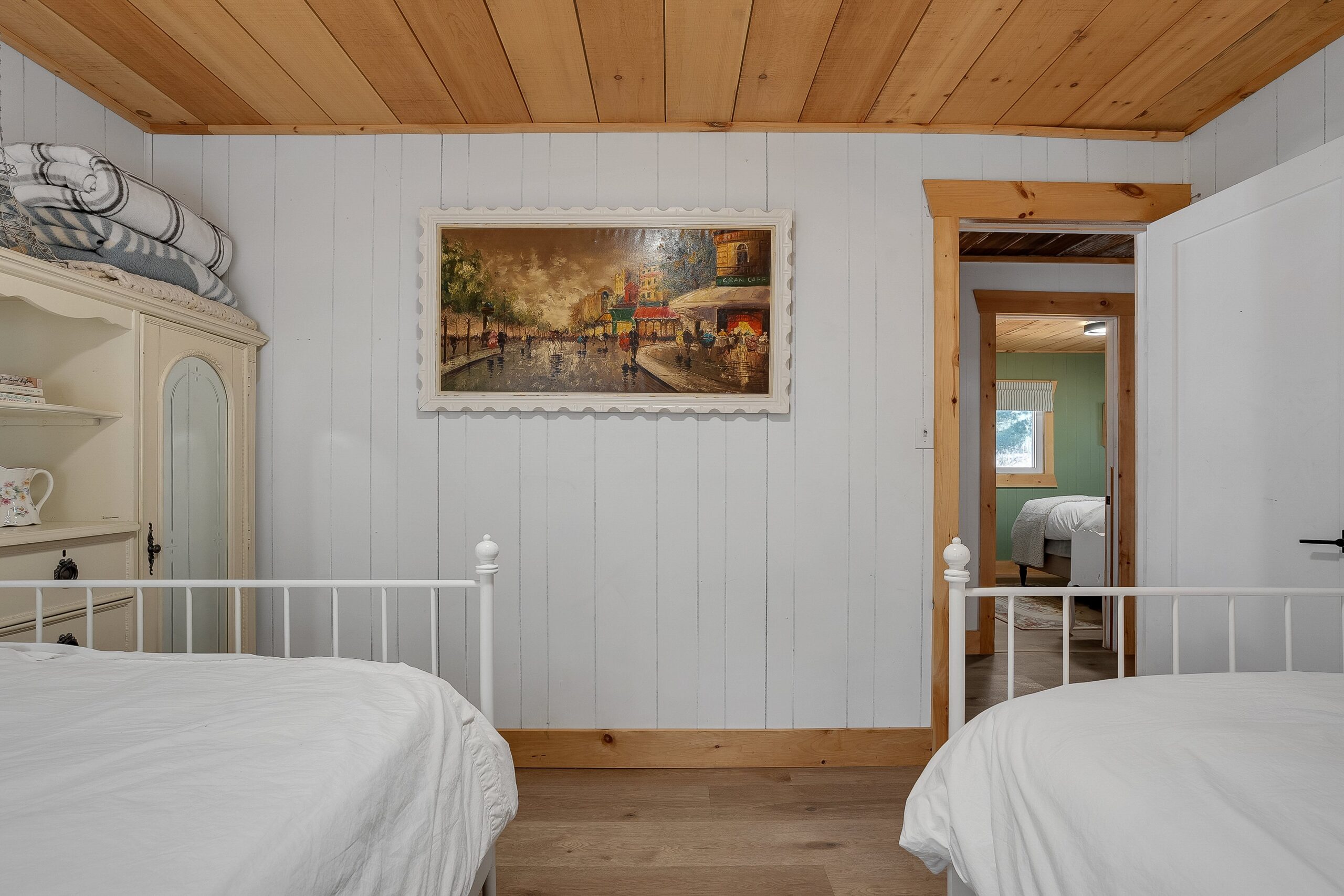 The ends of two white beds face a white wall with a painting