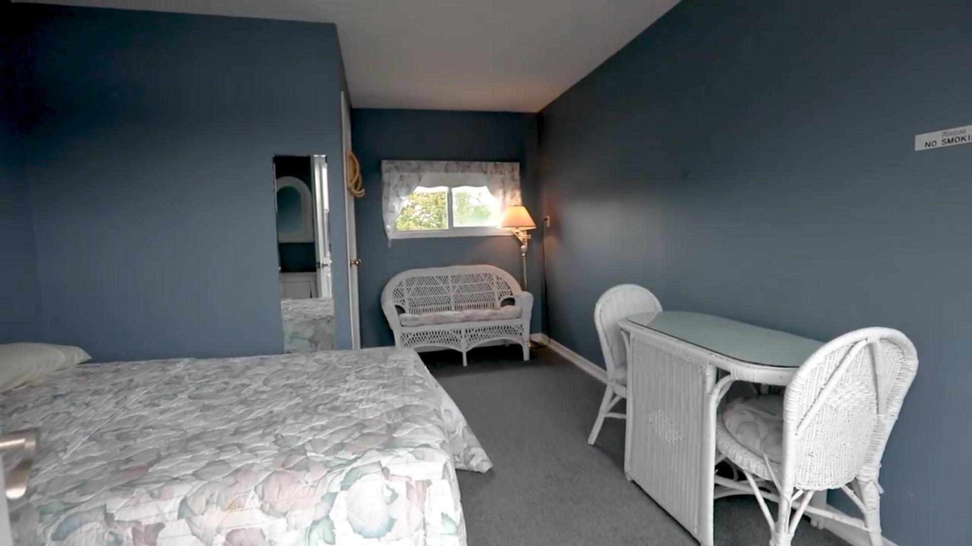 A grey-blue painted room with a white floral bed and a white wicker chair