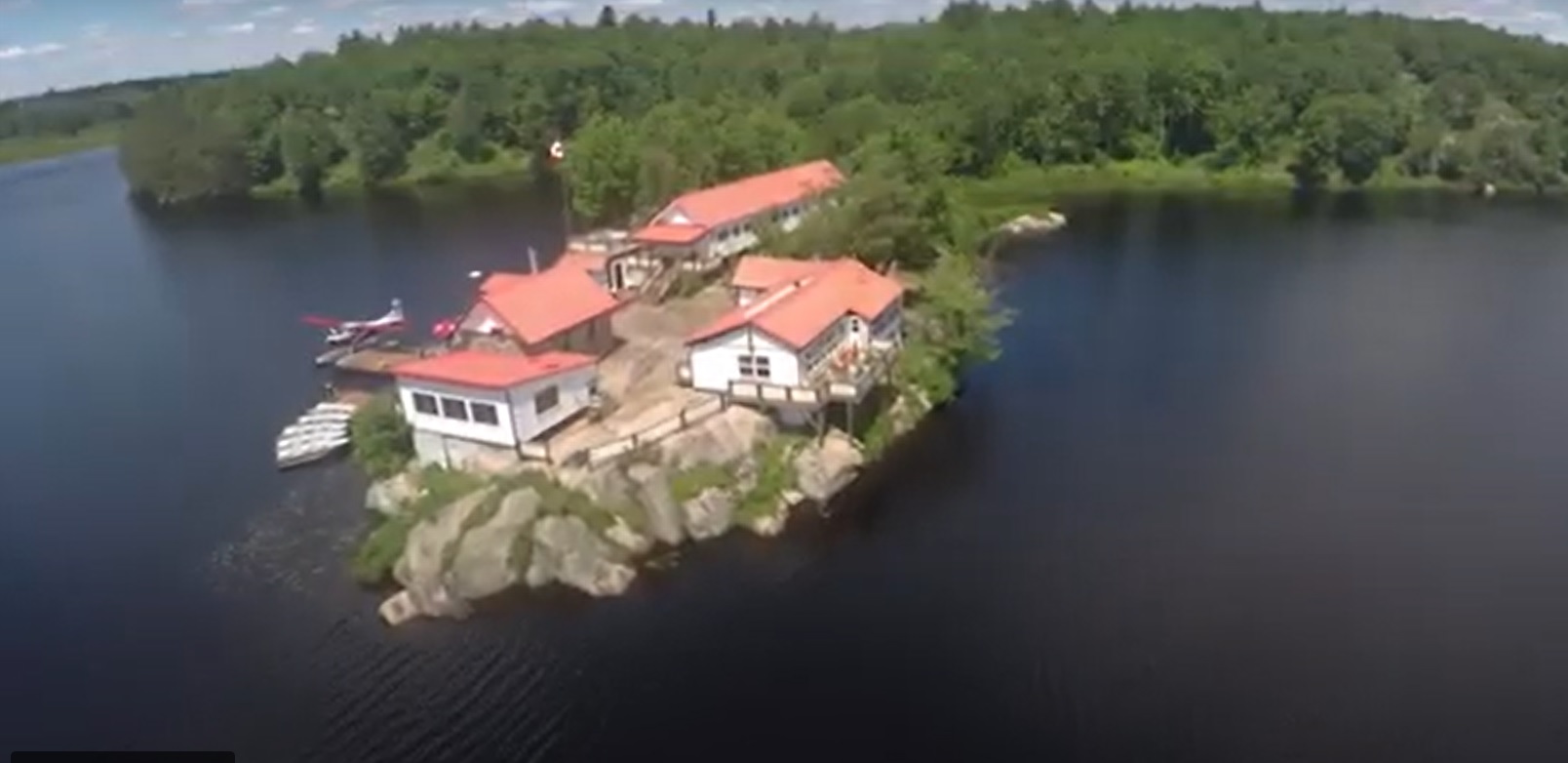 Aerial view of a sprawling white lodge with a red roof on the water