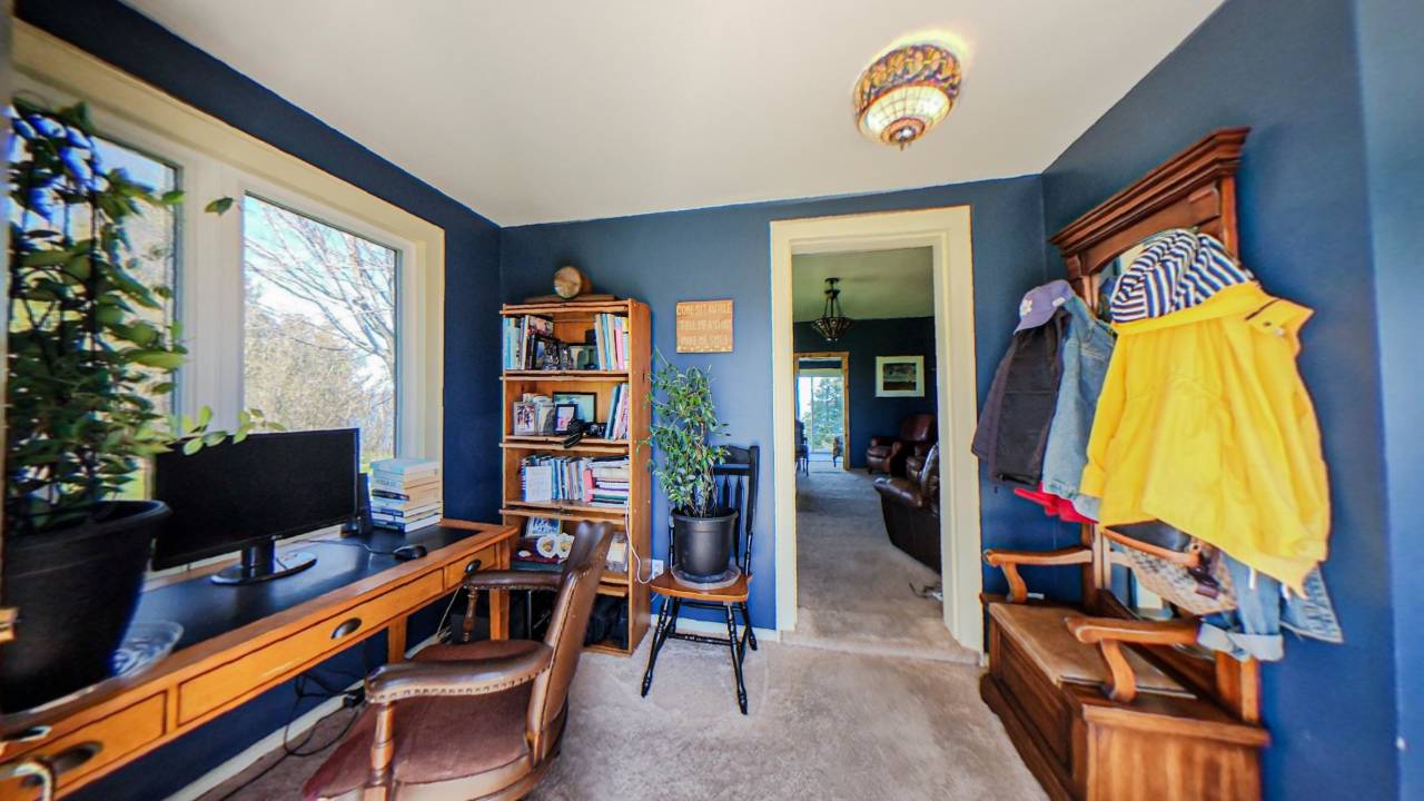 a blue painted room with an open doorway. A wood desk with a wood chair faces the left window. bEHIND, A COAT RACK
