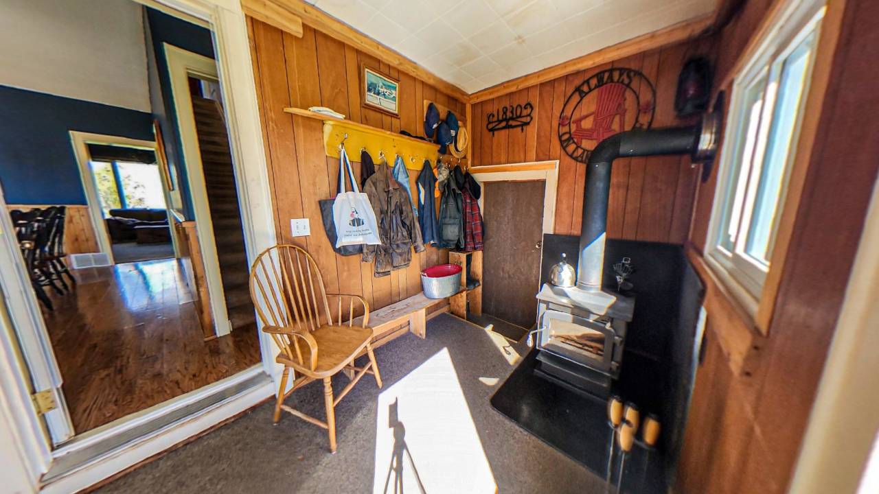 A wood panelled room with hanging coats and a wood stove. To the left, a step that leads into the rest of hte house