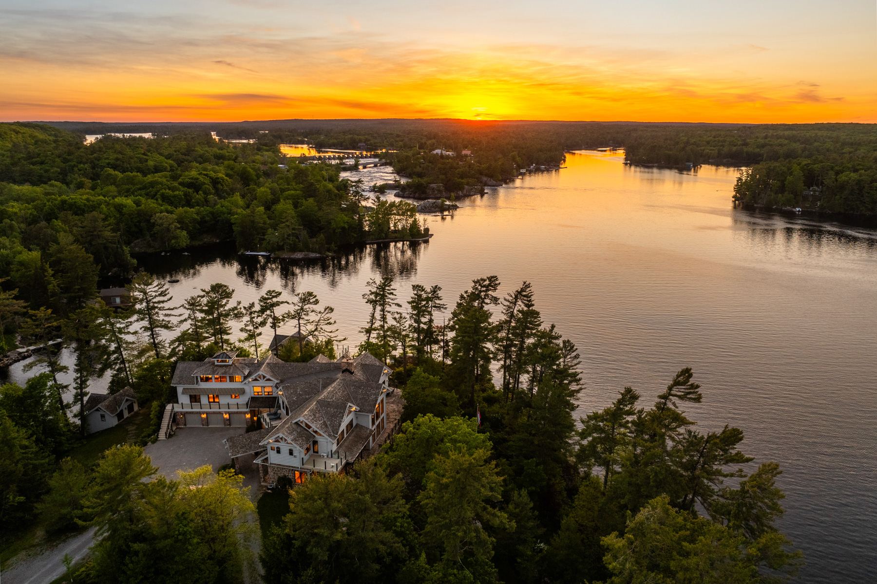 A large property surrounded by trees nearby a lake at sunset