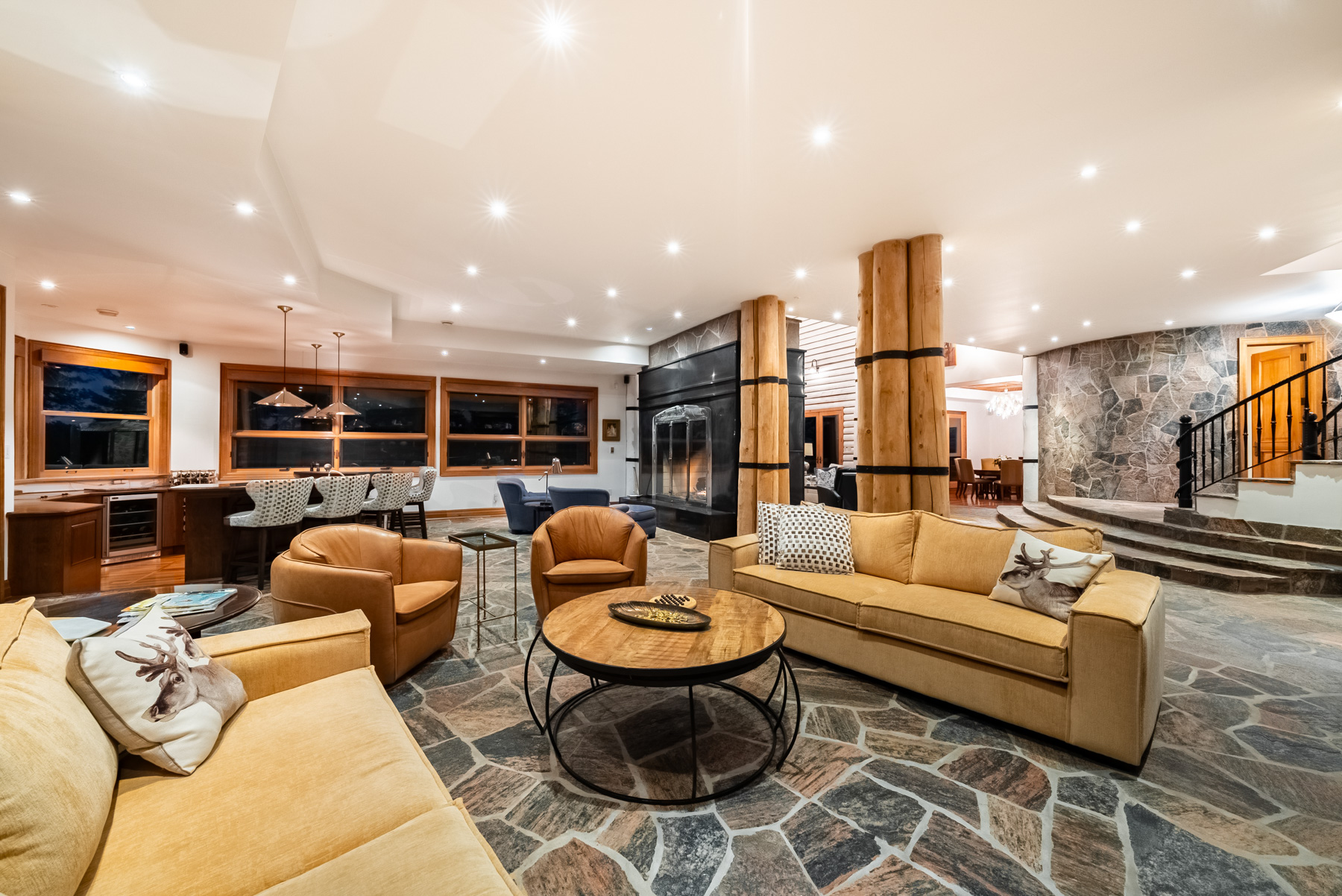 On stone floors, a seating area with couches and chairs around a small, wood, round table