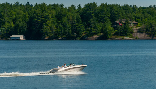 Boat moving along on Lake Muskoka lined with cottages and boathouses