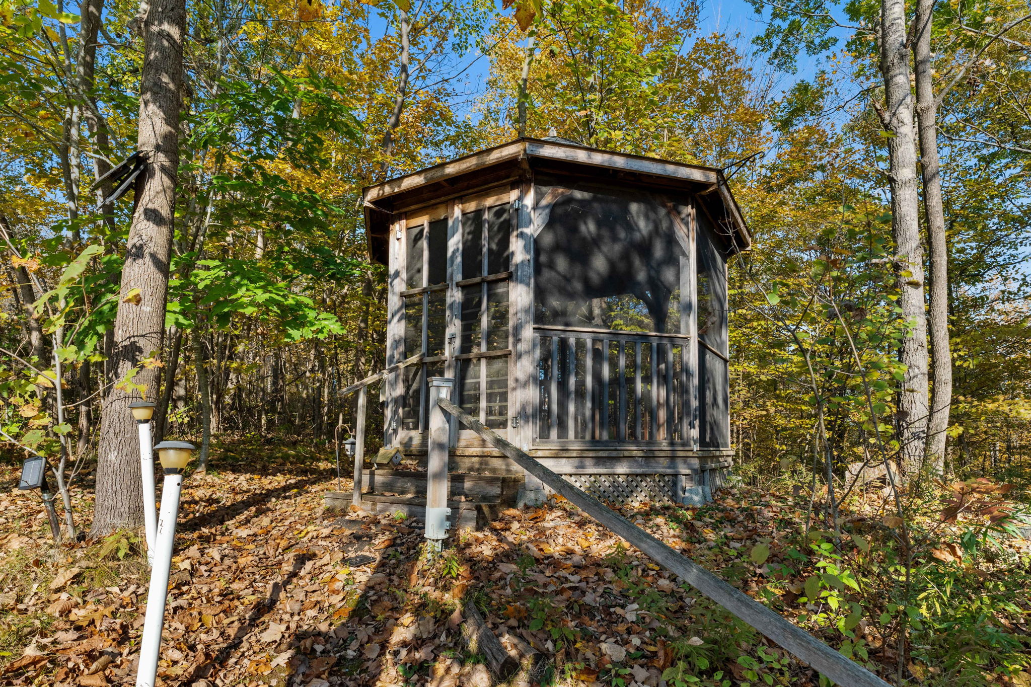 A small grey gazebo on a leafy hillside