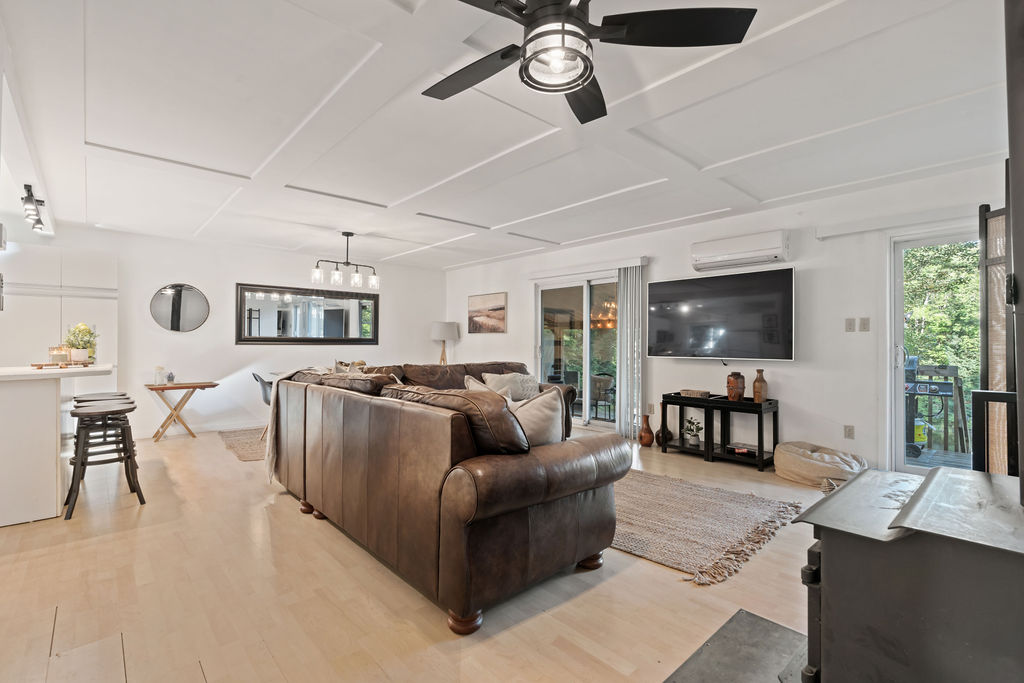 A brown leather couch faces a sliding glass door and a flatscreen TV