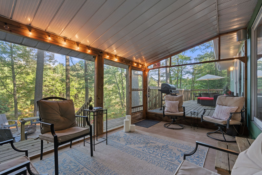 Chairs sit in a small screened in porch with white fairy lights