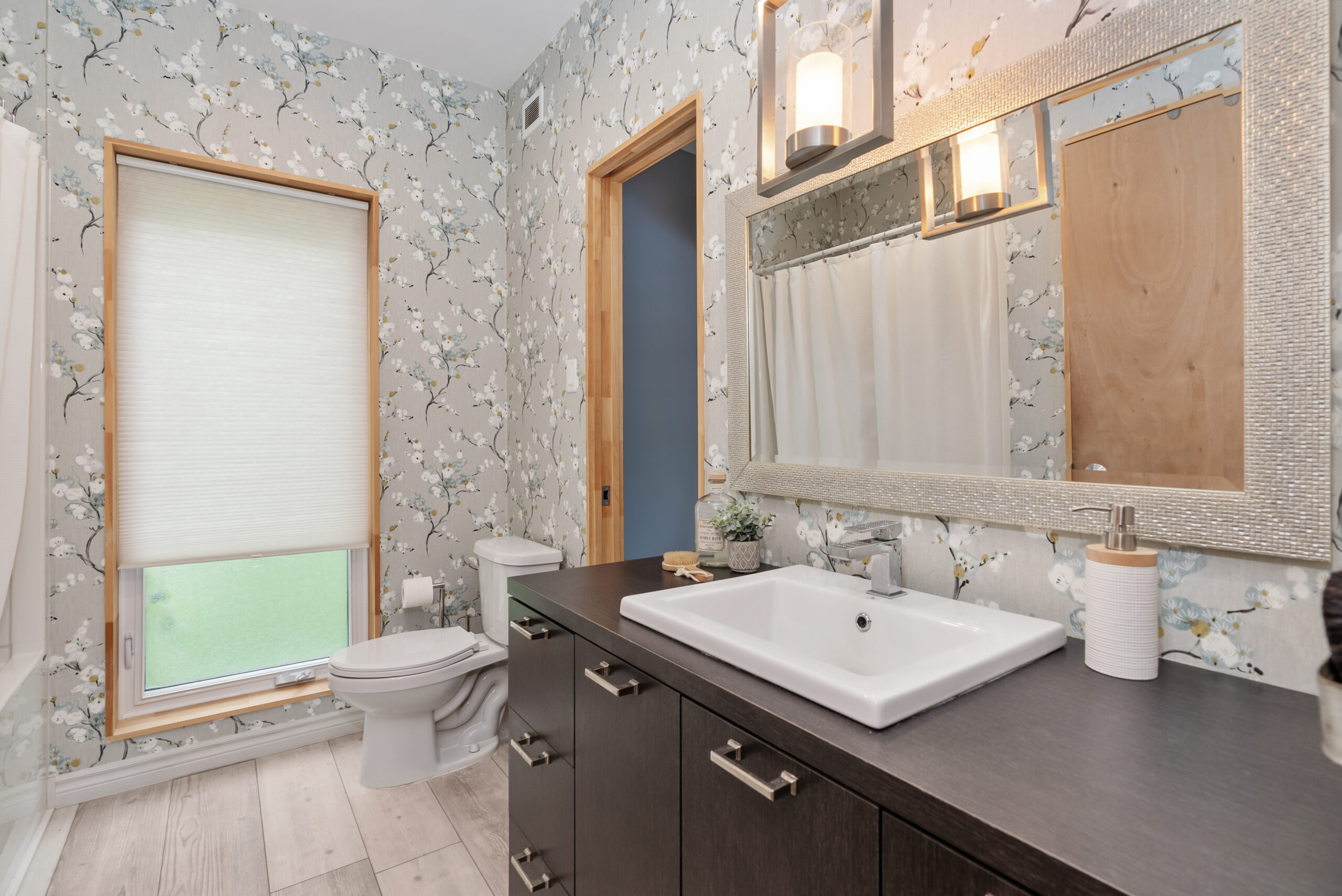 A white toilet next to a brown vanity in a wallpapered room