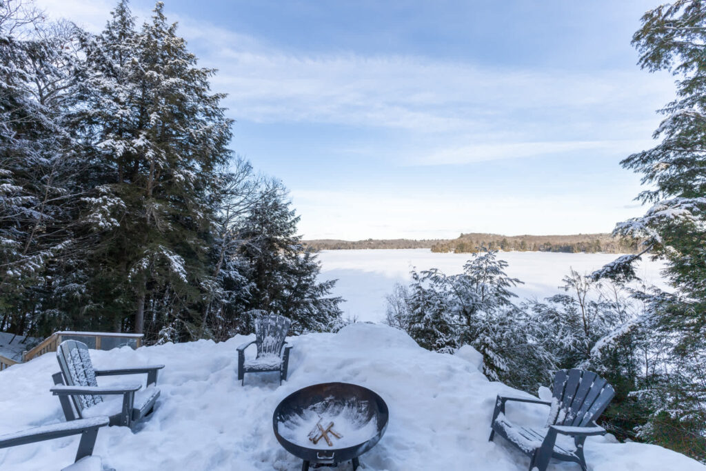 A fire pit in the snow with the lake in the distance