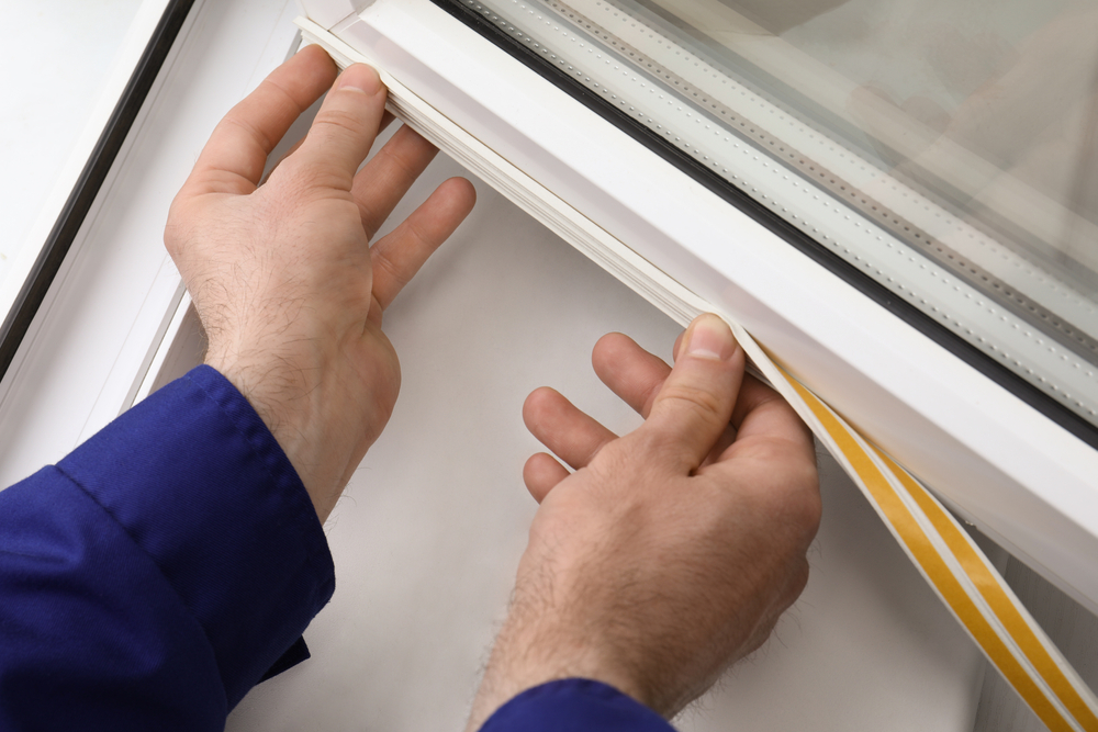Someone sealing a window with weatherstripping