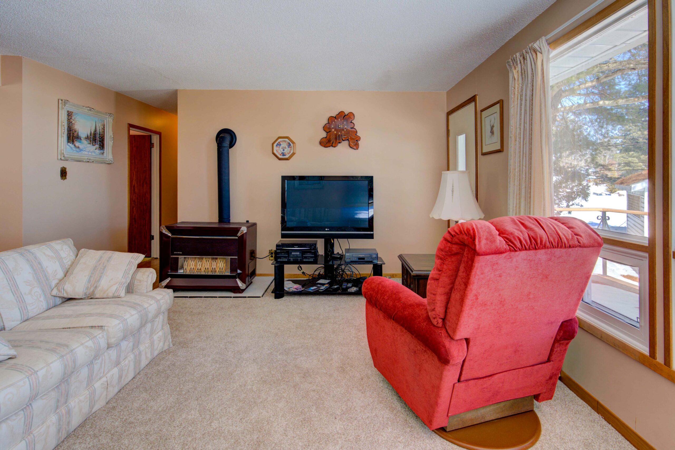A red chair faces a TV and wood stove