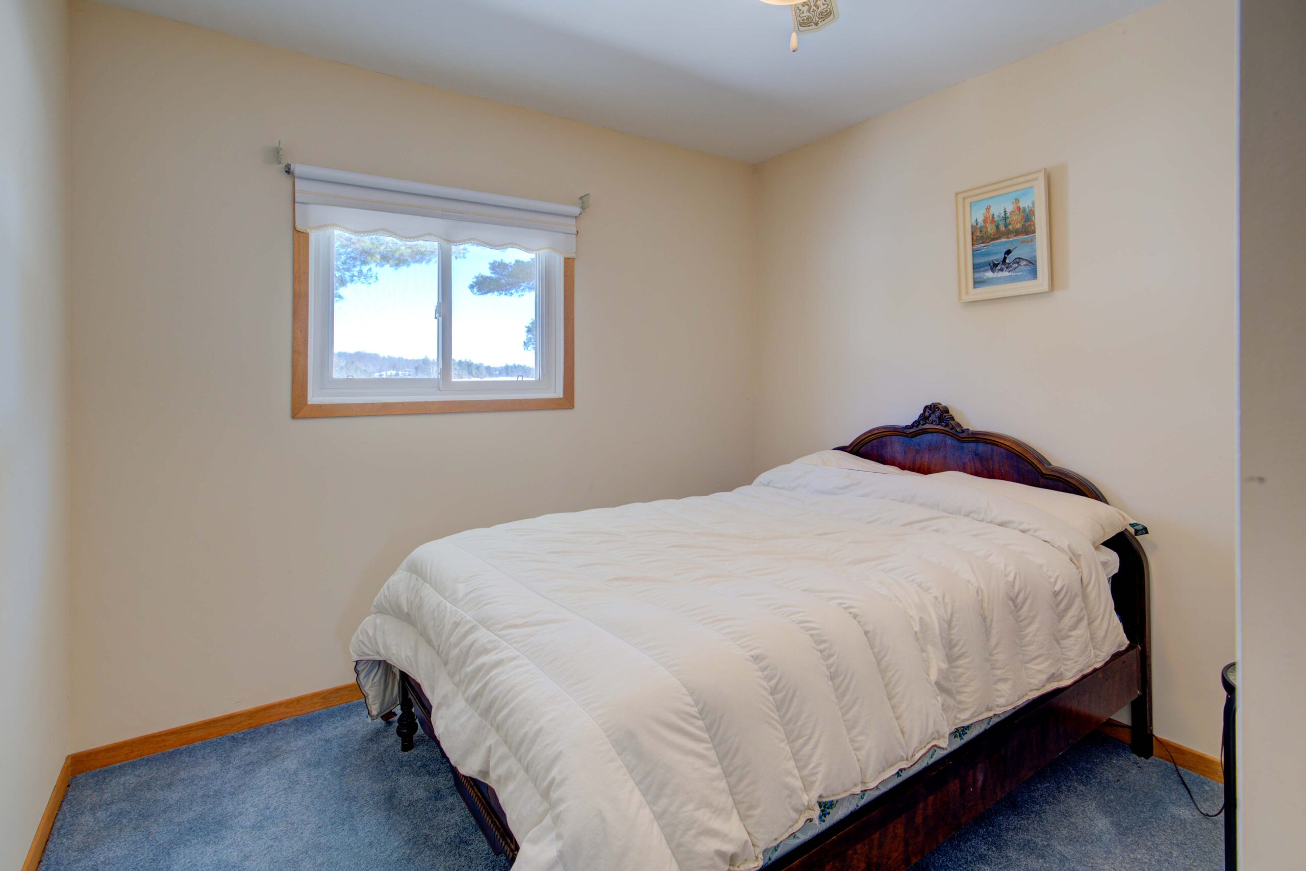 A bed with a white duvet in a white room with a blue carpet