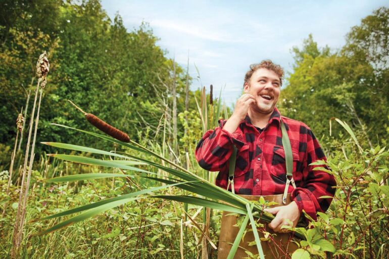 A man standing in a field wearing a red, plaid shirt