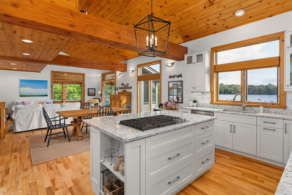 Combined kitchen, dining, and living space with large windows and natural wood accents