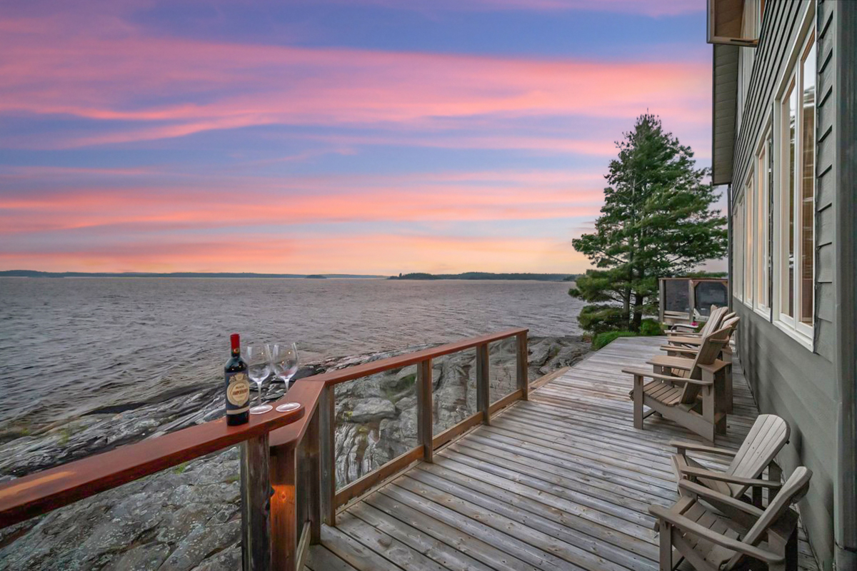 Deck overlooking Georgian Bay at sunset with chairs and a bottle of wine on the railing