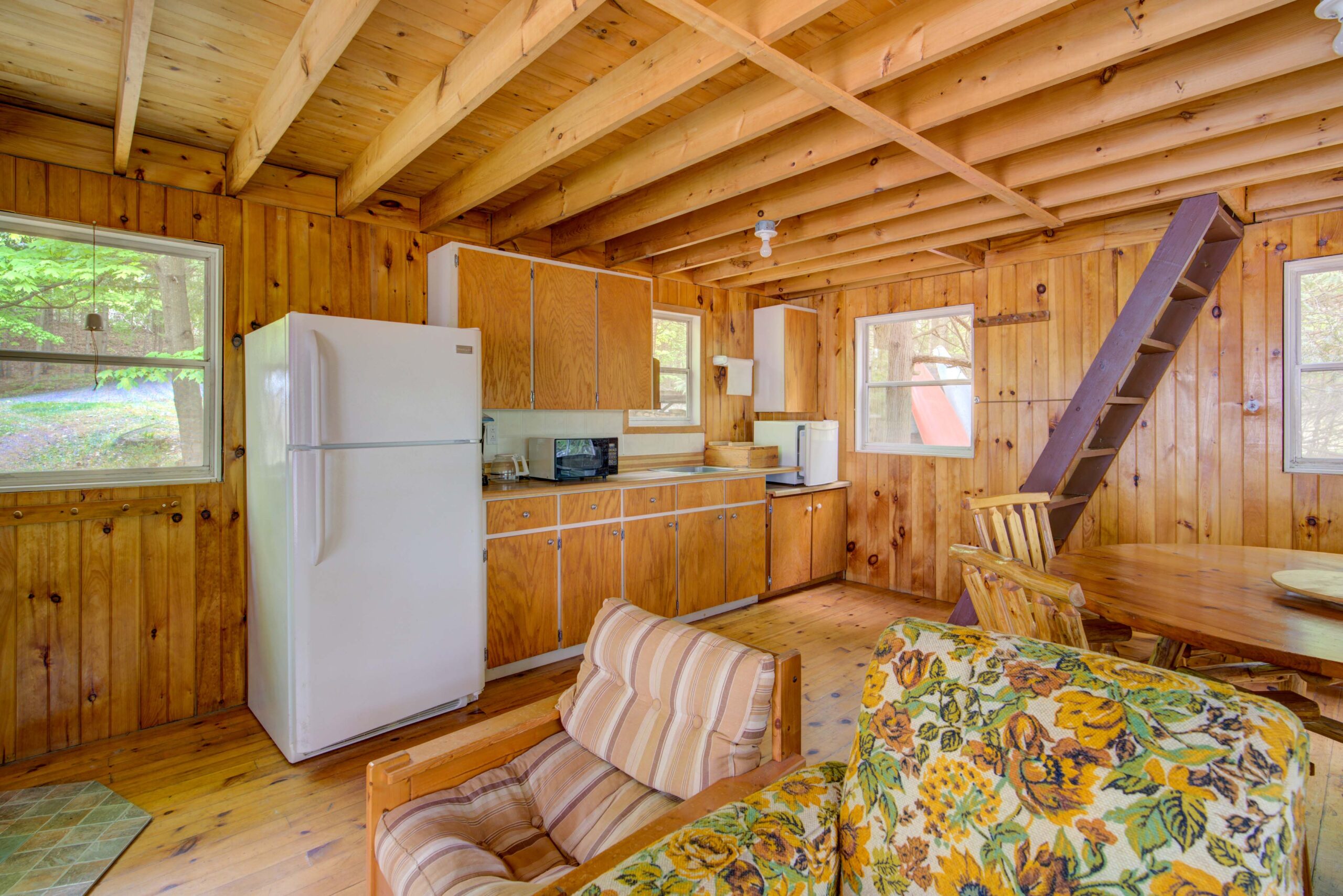 The inside of a wood cabin with mismatched furniture and a wall of wood cabinets