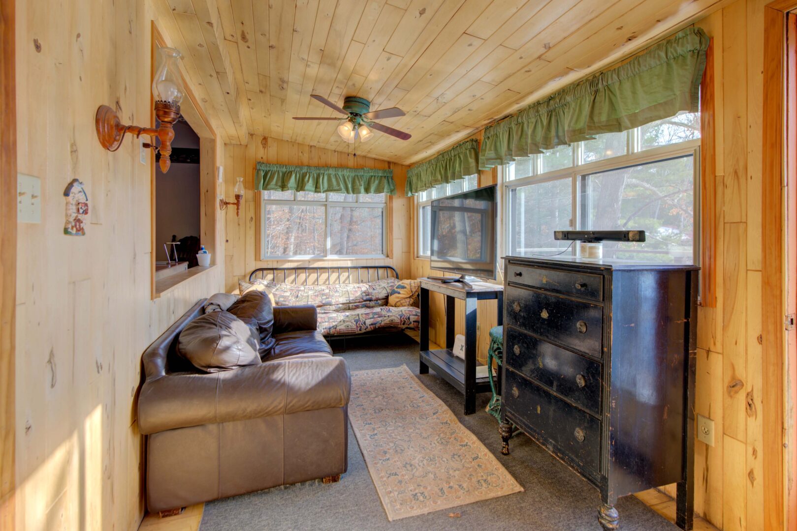 A beige couch faces a TV and a black cabinet in a sunroom