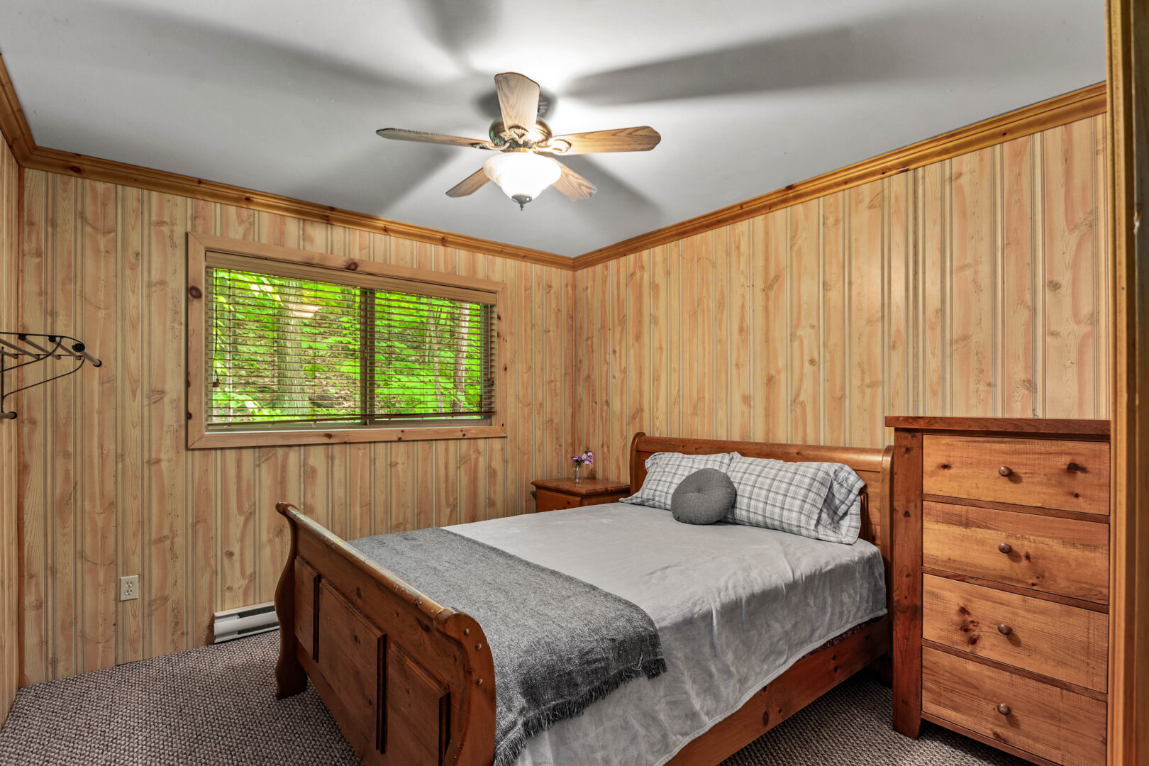 A wood sled bed with grey bedding in a wood paneled room