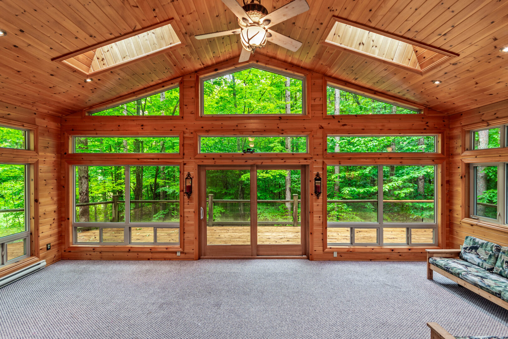 An empty living room with cathedral windows faces a forest