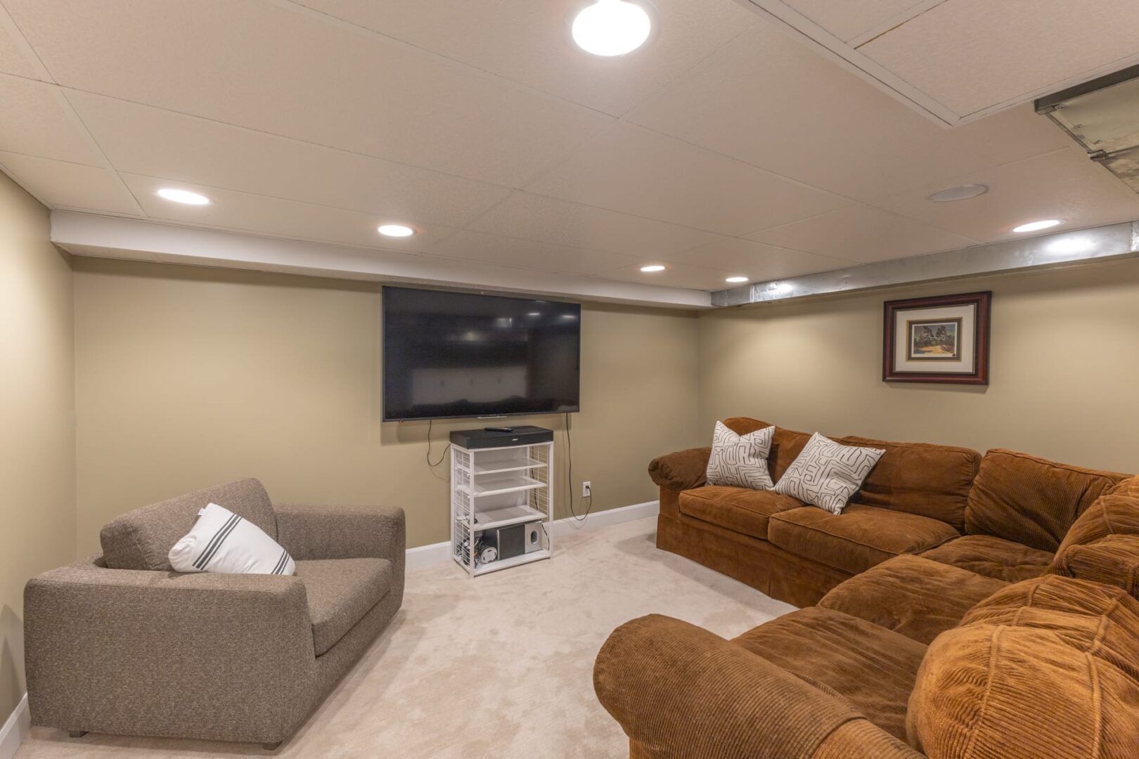 A grey basement living room with brown suede couches facing a TV