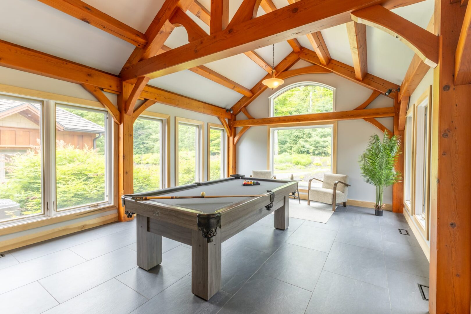 A pool table in a bright white room with wood beams and floor-to-ceiling windows