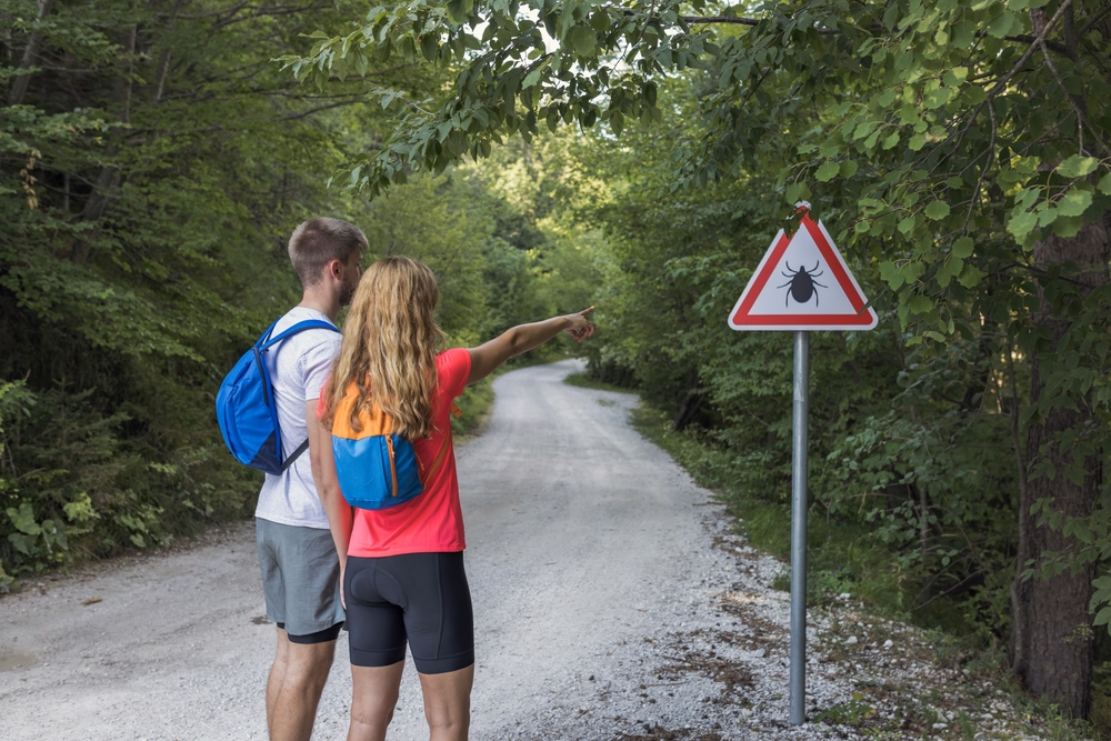 Two people pointing at a sign for ticks